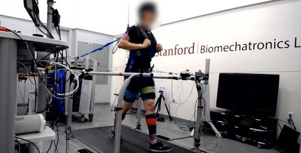 A photograph of subject running on a treadmill while wearing a safety harness, perturbation harness, motion capture markers and EMG sensors. Subject provided permission for photograph use and their face is blurred to preserve anonymity. 